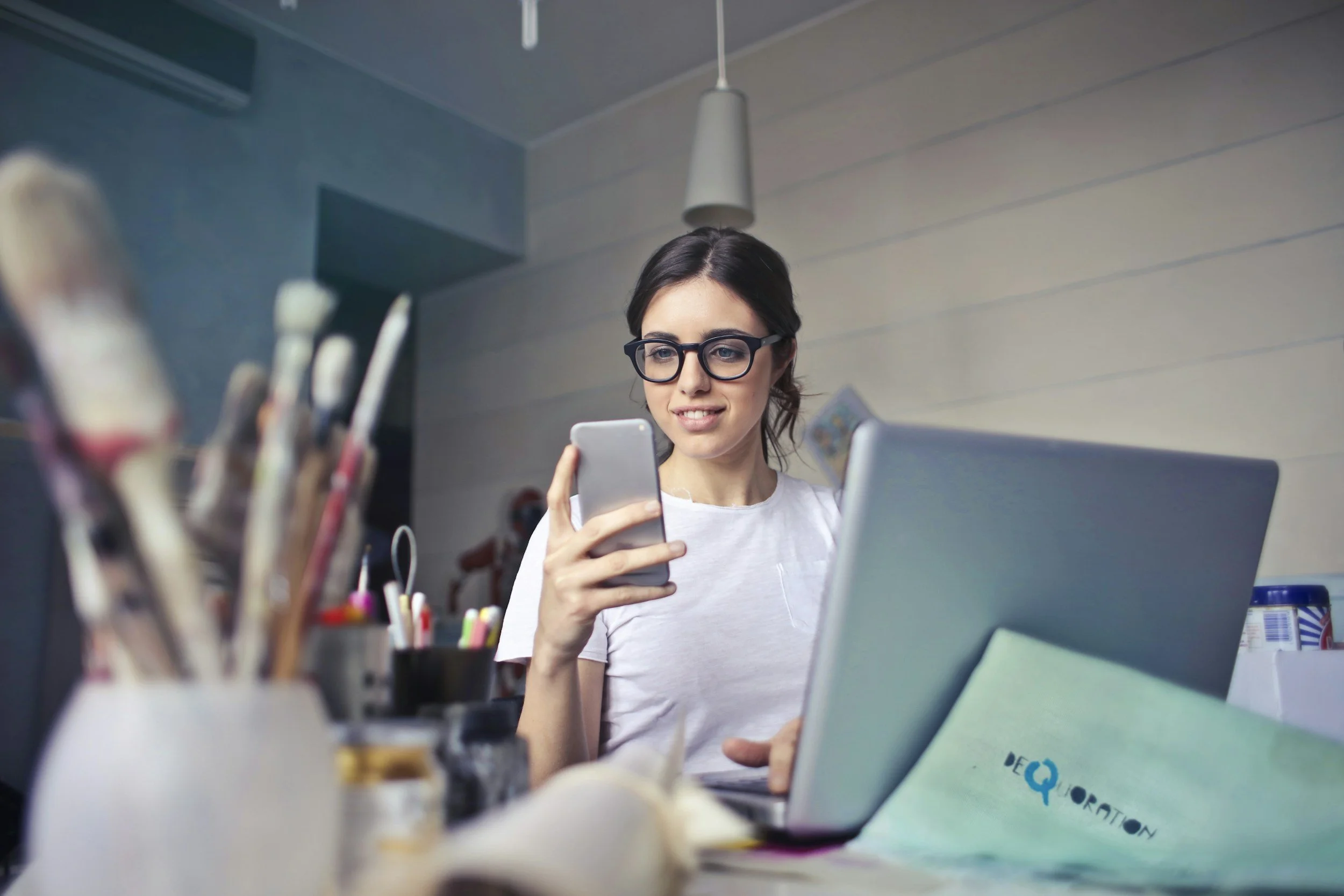 Woman at a desk looking at her phone surrounded by art supplies